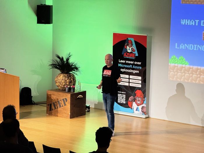 A speaker on stage beside the APE beach flag in the Auditorium